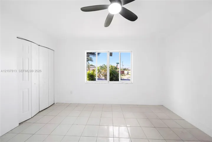 Interior space featuring neutral tile flooring, a multi-panel closet, a single window, and a ceiling-mounted fan with an integrated light fixture