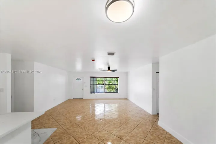 Open-concept interior featuring neutral wall finishes, tile flooring laid on a diagonal, a ceiling-mounted light fixture, a central ceiling fan, and a single-light entry door