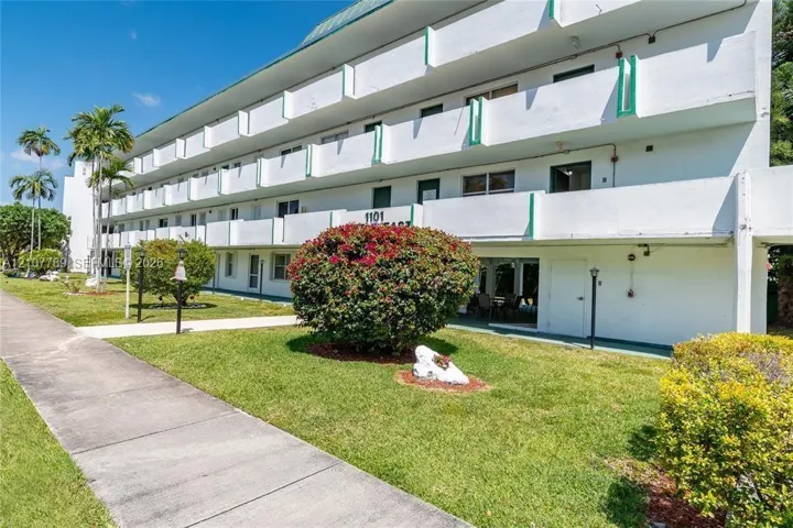 Multi-story exterior featuring white stucco facade, exterior balconies, concrete walkways, and manicured landscaping