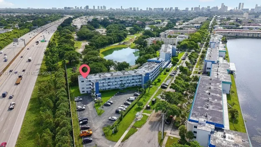 Aerial perspective featuring a multi-story residential building with dedicated surface parking, on-site pond, and proximity to major thoroughfares