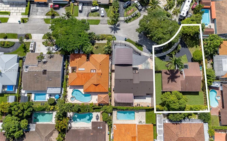 Aerial perspective of a property featuring a multi-pitched shingle roof, expansive manicured lawn, mature trees, and a private paved driveway