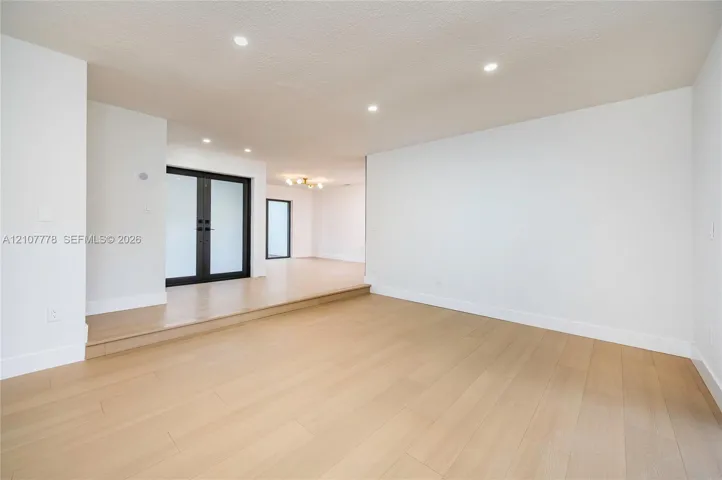 Interior space featuring wood-finish flooring, recessed lighting, and a tiered level design with black-framed double doors