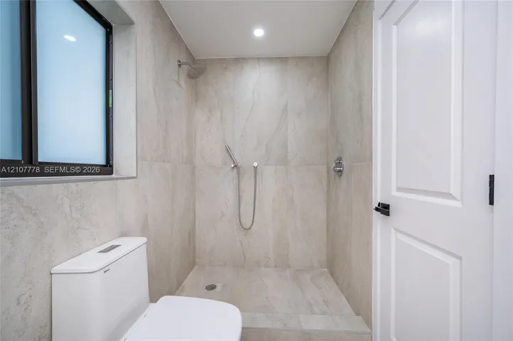 Walk-in shower featuring large-format neutral tile, a rainfall showerhead, a separate handheld sprayer, and a frosted window