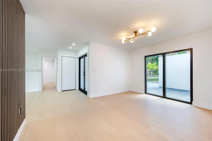 Light-filled interior featuring wood-finish flooring, a vertical slat wood accent wall, a multi-arm modern brass chandelier, and floor-to-ceiling glass sliding doors