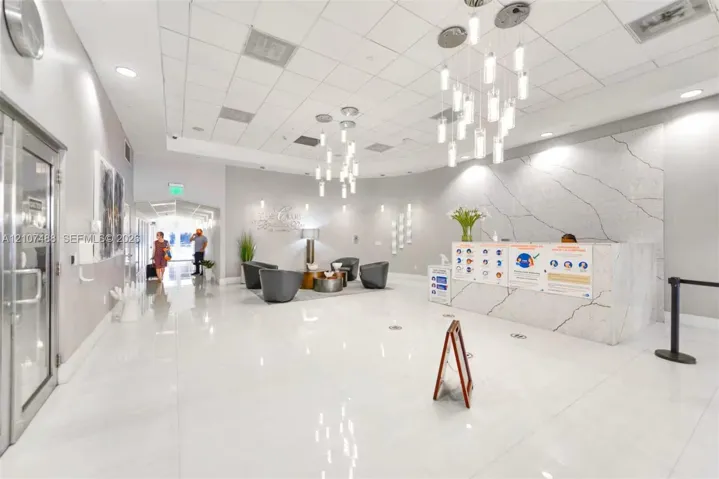 Lobby featuring high-gloss tile flooring, white stone-finish reception desk with dramatic veining, and modern multi-pendant lighting fixtures