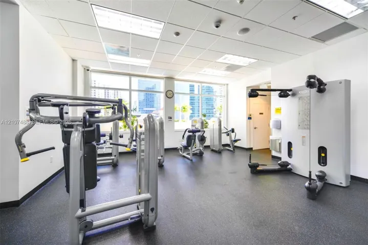 Fitness center featuring a rubberized floor surface, drop ceiling with recessed lighting, and expansive windows