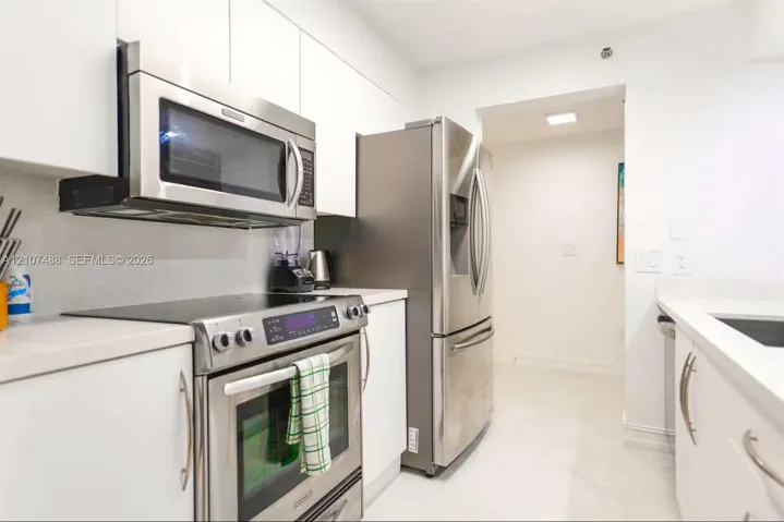 Kitchen featuring sleek white flat-panel cabinetry, light-toned countertops, and stainless steel appliances, including an over-the-range microwave and a bottom-freezer refrigerator
