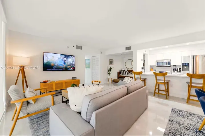Open-concept living space featuring high-gloss tile flooring, recessed lighting, white cabinetry, and a breakfast bar