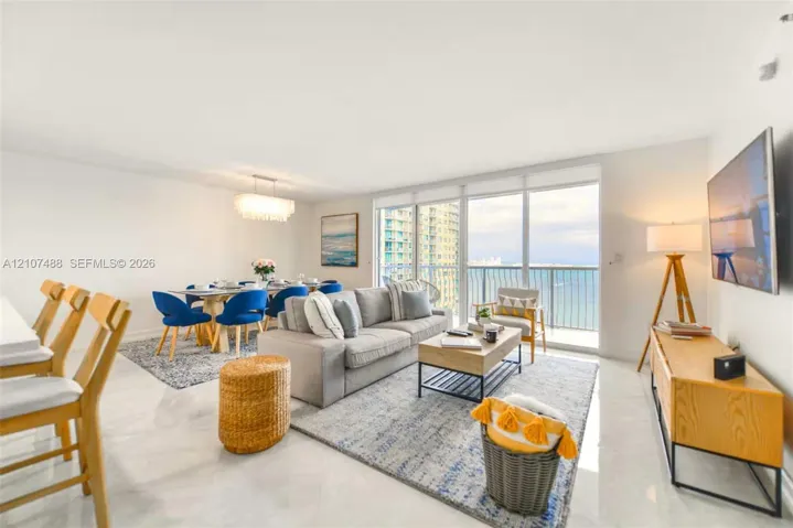 Open-concept main living area featuring light-toned tile flooring, floor-to-ceiling glass sliding doors, and a private balcony