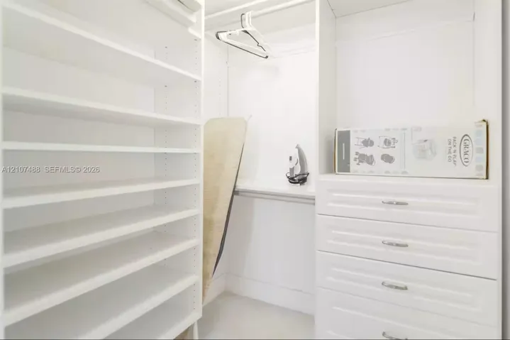Custom built-in closet featuring white cabinetry, floor-to-ceiling adjustable shelving, integrated storage drawers with metal hardware, and overhead hanging rods