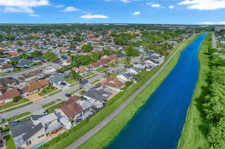 Aerial view of residential properties bordering a linear canal with paved walking path and mature landscaping