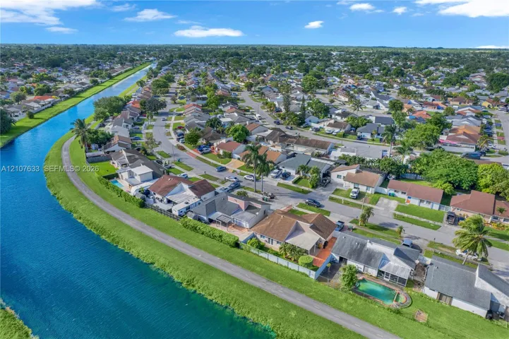 Aerial perspective of a waterfront residential neighborhood featuring a canal, paved perimeter pathways, and mature palm trees