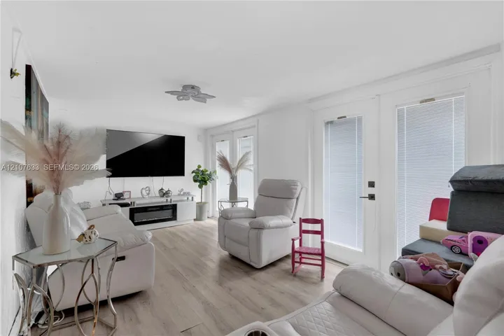 Living area featuring light-toned wood-finish flooring, recessed lighting, and dual glass-paned doors with integrated blinds