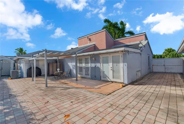 Exterior space featuring a paved patio, retractable fabric canopy, double glass-paneled doors, and full perimeter fencing