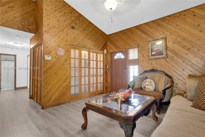 Vaulted ceiling with wood-plank paneled walls, wood-finish flooring, multi-pane glass sliding doors, and a paneled entry door with sidelight