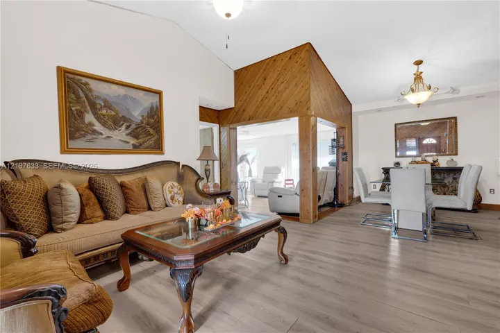 Vaulted ceilings, wood-finish flooring, wood-paneled accent wall, and decorative chandelier lighting