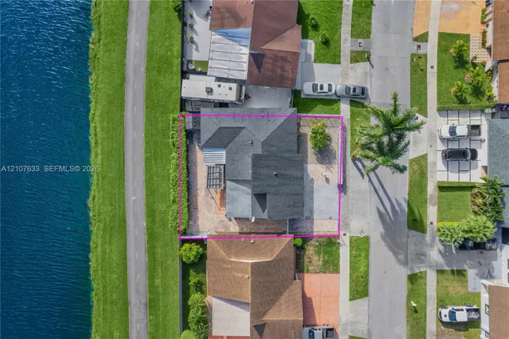 Aerial perspective of a waterfront property featuring a multi-pitched shingled roof, a paved hardscaped exterior, a pergola, and mature perimeter landscaping