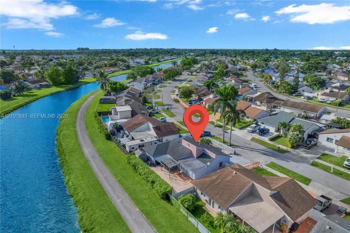 Aerial perspective of a property featuring direct canal frontage, a paved rear patio, a pergola, and a multi-pitched roofline