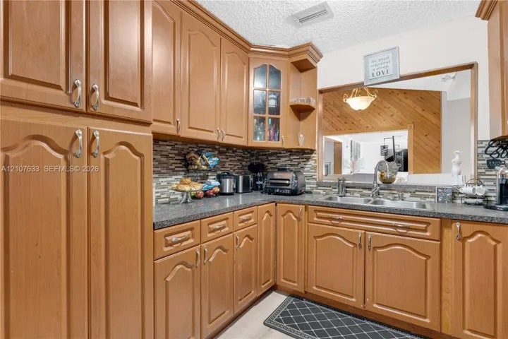 Kitchen featuring wood cabinetry with arched detailing, glass-front upper cabinet, dark stone-finish countertops, mosaic tile backsplash, and a dual-basin stainless steel sink