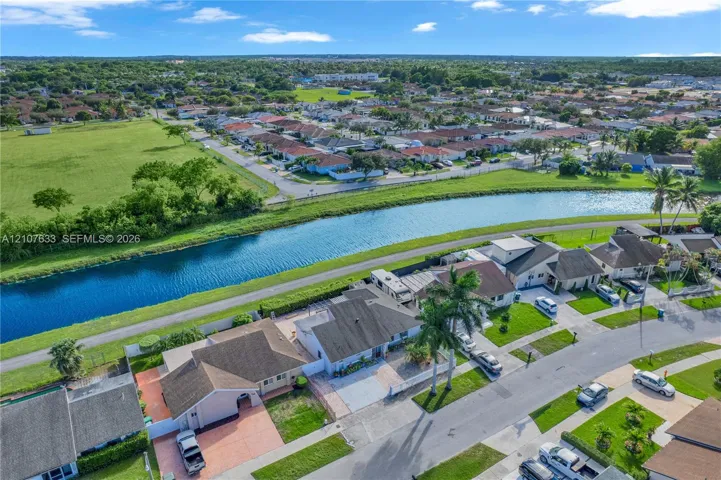 Aerial perspective featuring a waterfront property with a concrete tile roof, paved driveway, and mature palm trees
