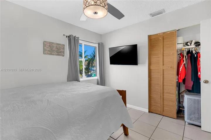 Ceramic tile flooring, louvered bi-fold closet doors, and a ceiling-mounted light fixture with a decorative drum shade