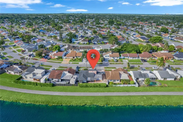 Aerial perspective featuring a waterfront property with a concrete patio, perimeter shrubbery, and shingle roofing