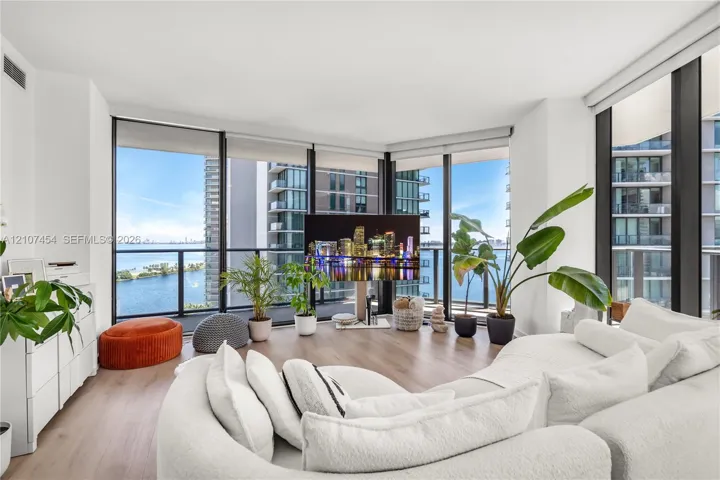 Floor-to-ceiling windows, wood-finish flooring, and black metal-framed balcony access with a glass railing