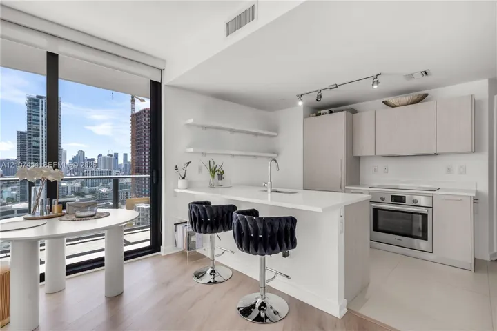 Kitchen featuring a quartz-topped island, light wood-finish cabinetry, built-in stainless steel oven, floor-to-ceiling windows, and floating shelving