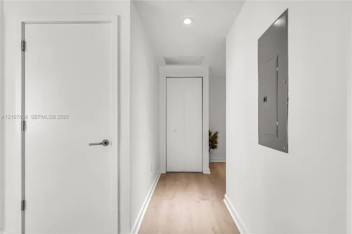 Hallway featuring light wood-finish flooring, white panel doors, recessed ceiling lighting, and a bifold closet door