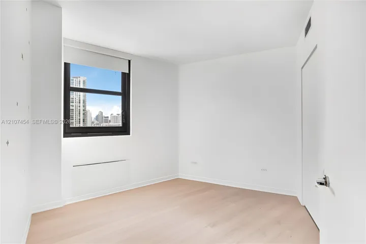 Light-filled interior featuring wood-finish flooring, a large window with urban skyline exposure, and clean, neutral wall finishes
