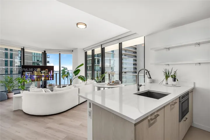 Kitchen featuring a white quartz countertop, undermount sink, gooseneck faucet, light-finish cabinetry, and built-in microwave, complemented by wood-finish flooring and floor-to-ceiling windows