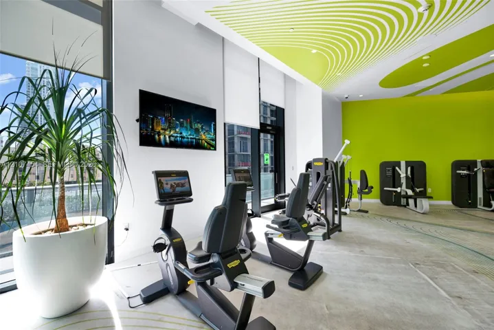 Fitness facility featuring floor-to-ceiling windows, high ceilings with decorative acoustic panels, polished concrete flooring, and wall-mounted television