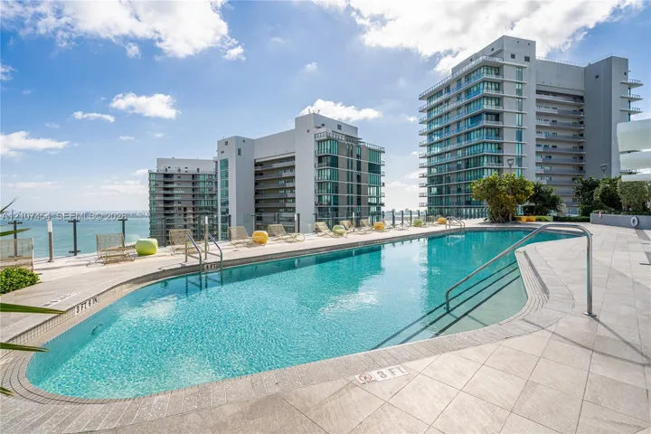 Curved swimming pool featuring a tile surround, metal handrails, and a glass panel perimeter fence
