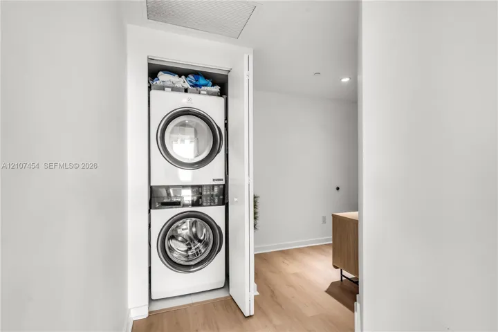 Stacked front-loading washer and dryer unit enclosed in a dedicated closet featuring light wood-finish flooring