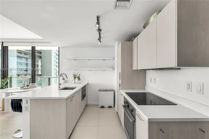 Kitchen featuring light wood-finish cabinetry, white solid-surface countertops, built-in cooktop, undermount stainless steel sink, and wall-mounted track lighting