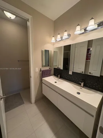 Floating dual-sink vanity with a seamless integrated basin, dark mosaic tile backsplash, large wall-mounted mirror, and multi-bulb polished chrome vanity lighting