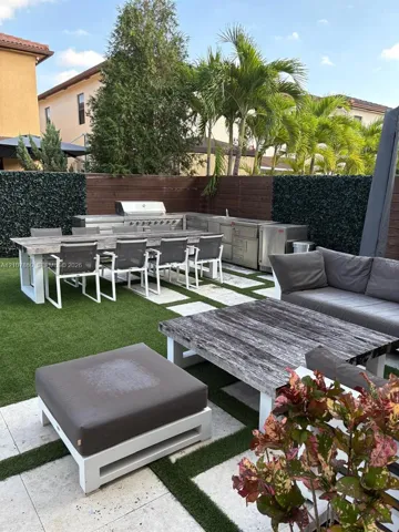 Outdoor kitchen featuring stainless steel appliances and a built-in grill, complemented by paver stone hardscaping, artificial turf, and wood privacy fencing