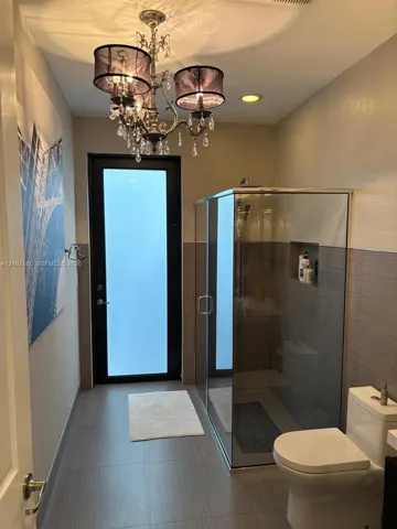 Bathroom featuring a walk-in glass-enclosed shower with a recessed wall niche, dual-tone tiled wall finish, frosted-glass exterior door, and ornate crystal chandelier lighting