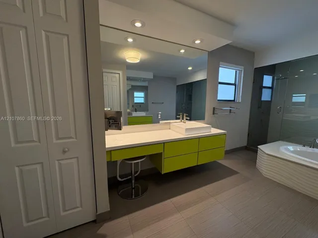 Floating vanity with a rectangular vessel sink and solid-surface countertop, full-width mirror, recessed lighting, tile flooring, and a glass-enclosed shower with a soaking tub