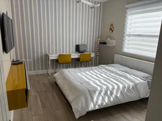 Wood-finish flooring, vertical-striped accent wall, built-in mustard-tone wall cabinetry, and light-filtering horizontal window shades