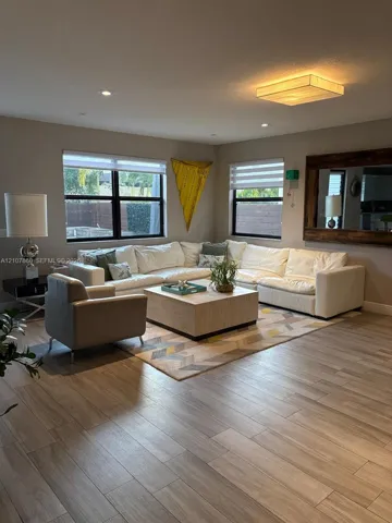 Wood-finish tile flooring, recessed lighting, large rectangular flush-mount ceiling fixture, dual-pane windows with black frames, and a large wall-mounted mirror with a wide wood frame