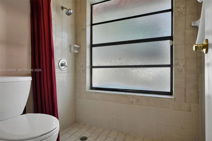 Bathroom featuring tiled wall and floor surfaces, a metal-framed window with frosted glass, a wall-mounted shower fixture, and a built-in soap dish
