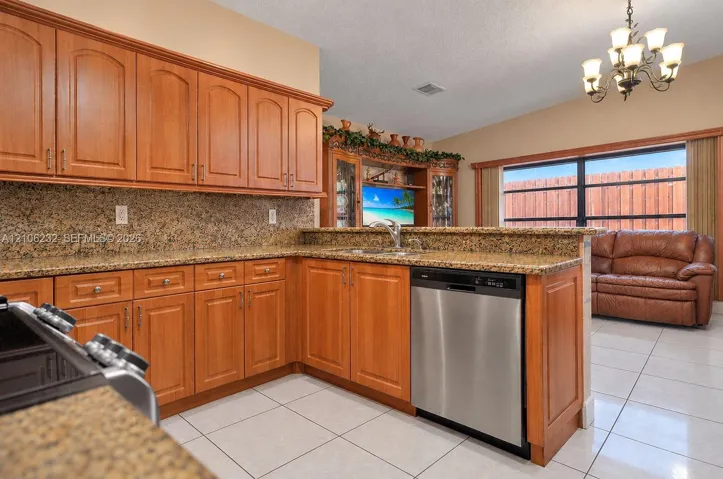 Kitchen featuring natural wood cabinetry, stone-surface countertops, built-in cabinetry, stainless steel dishwasher, and a chandelier
