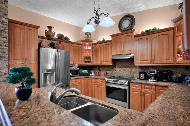 Kitchen featuring wood cabinetry, stone countertops, stainless steel appliances, a dual-basin stainless steel sink, and a decorative chandelier