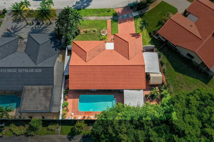 Aerial view featuring a terracotta-tiled roof, an inground swimming pool, a paved walkway, and mature landscaping