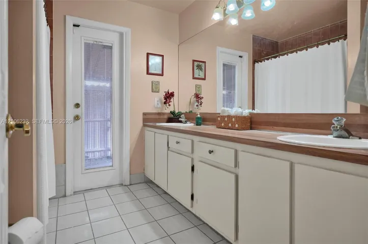 Dual vanity featuring white cabinetry, integrated sinks, a wood-finish countertop, full-width wall mirror, and ceramic tile flooring