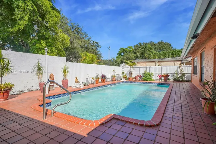 In-ground swimming pool with tile trim, complemented by a surrounding clay-tile patio and white privacy fencing