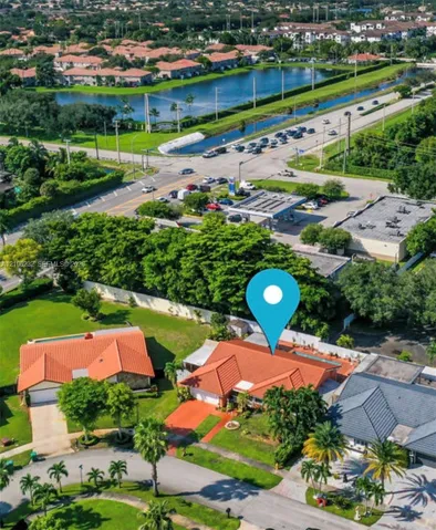 Aerial perspective featuring a terracotta-tiled roof, multi-car garage, and landscaped grounds with mature palm trees
