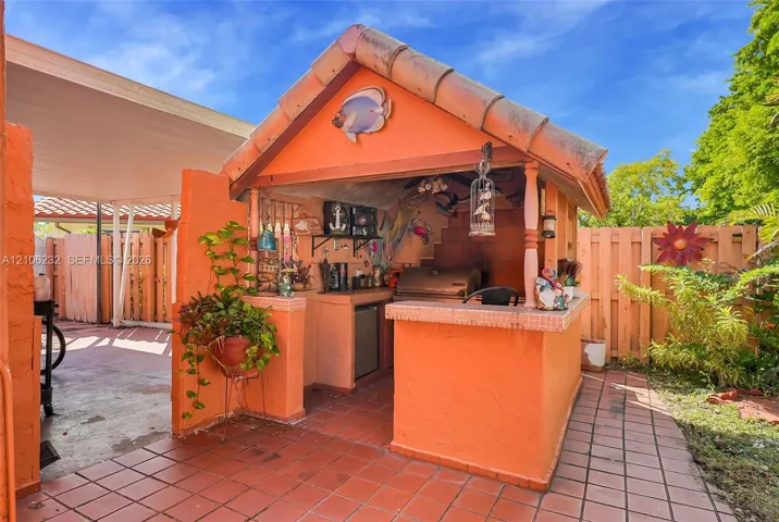 Outdoor kitchen featuring a built-in grill, tiled countertop, under-counter refrigeration, and a gabled roof structure with terra cotta tiling