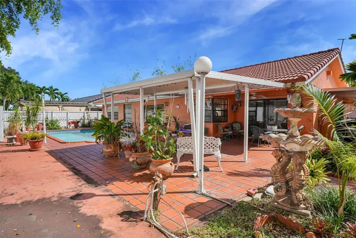 Rear exterior featuring a covered patio with tiled flooring, a built-in swimming pool, and a white privacy fence